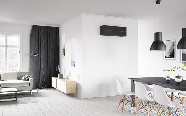 sort varmepumpe som er montert på en hvit vegg i en stue med sofagruppe og spisestue med sort bord og hvite stoler og grå tregulv.